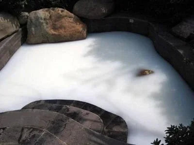 Outdoor jetted tub filled with foamy water, surrounded by stone landscaping
