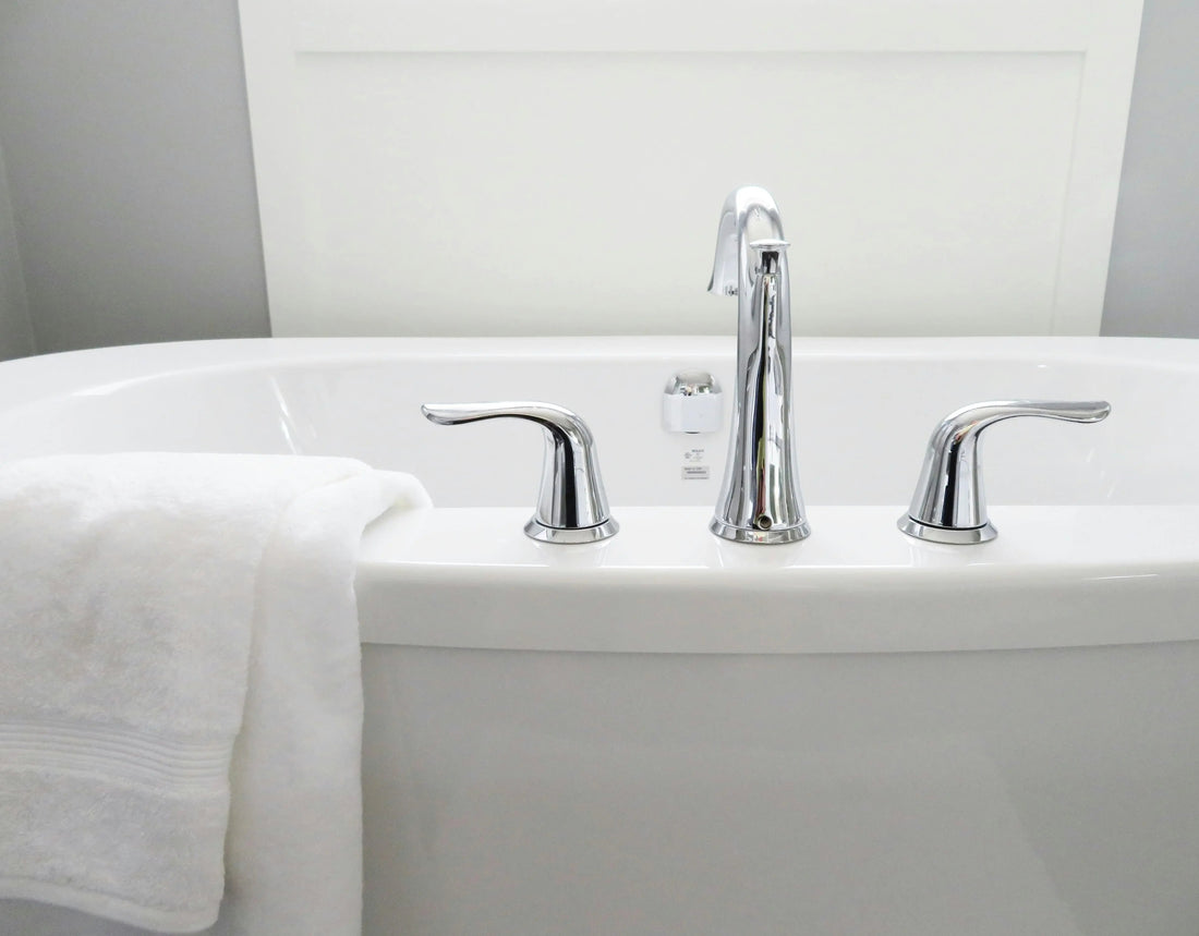 Modern jetted bathtub with chrome faucet, handles, and a white towel draped over the edge.